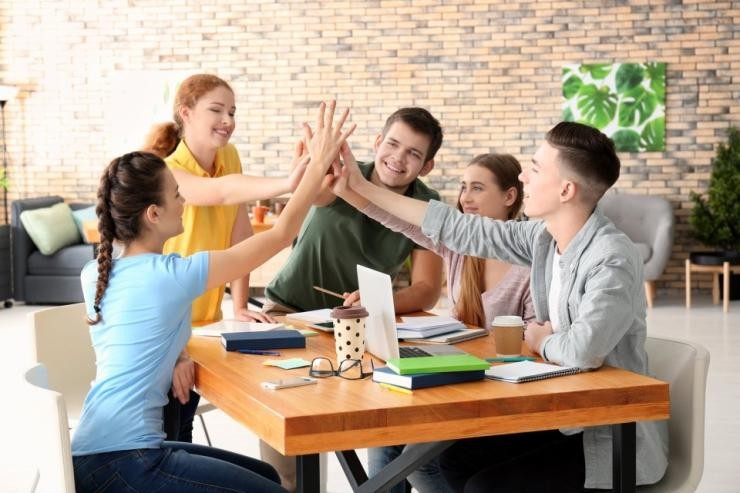 Jugendliche sitzen an einem Tisch und geben sich ein High-Five 